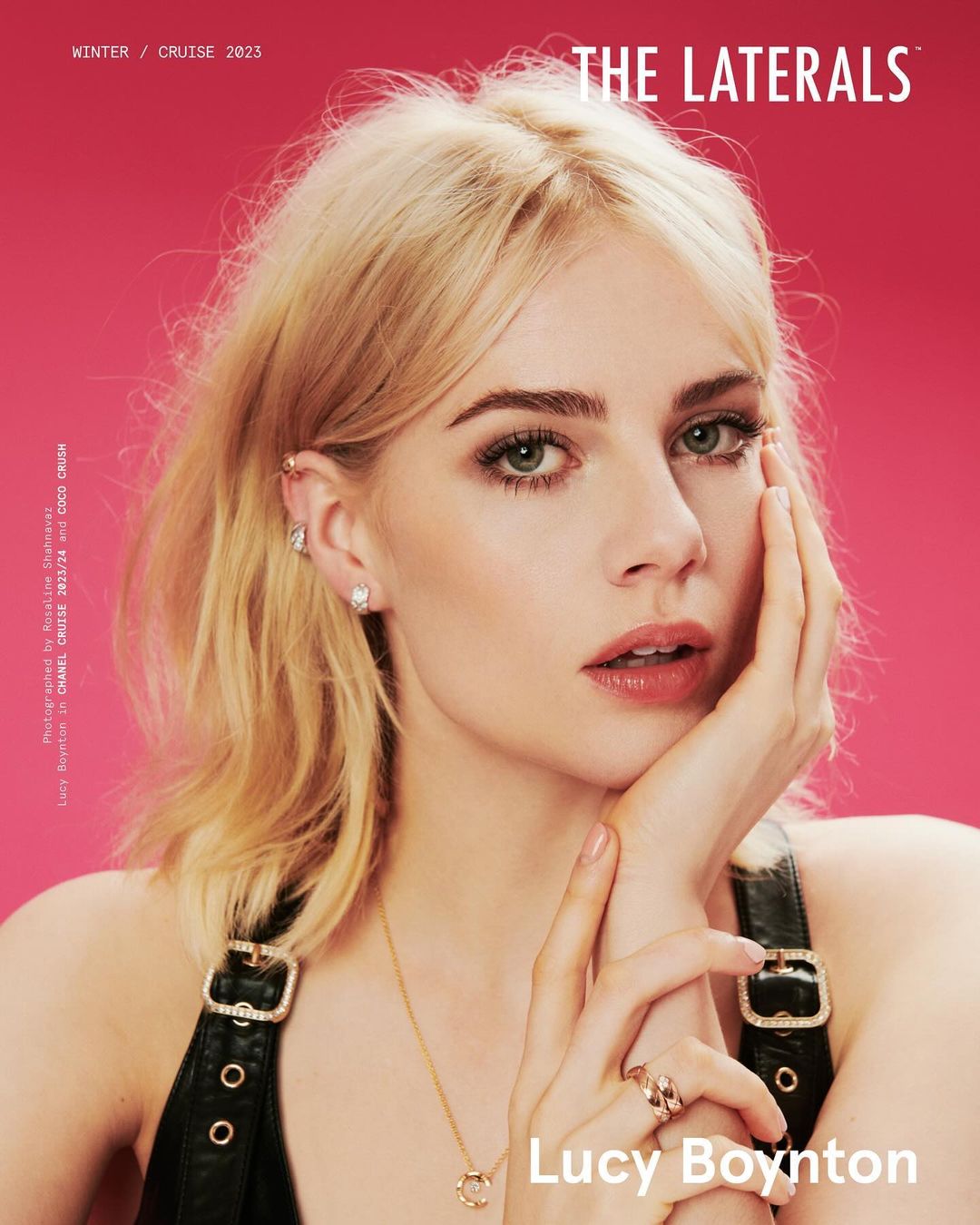 Close-up of Lucy Boynton with blonde wavy hair, wearing a black top and gold necklace on a pink background for The Laterals magazine.