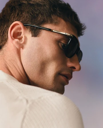 Profile portrait of a man wearing dark sunglasses and a light-coloured textured knit sweater against a gradient background.