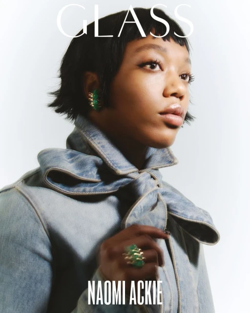 Portrait of Naomi Ackie wearing a denim jacket, green statement earrings, and ring against a white background with the text GLASS.
