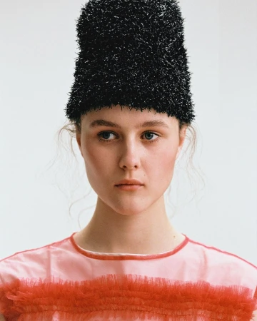 Portrait of a woman wearing a textured black tall hat and a pink top by Rosaline Shahnavaz