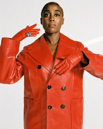 A portrait of an adult woman with short hair wearing a red leather jacket and gloves, accessorized with a statement ring, against white.