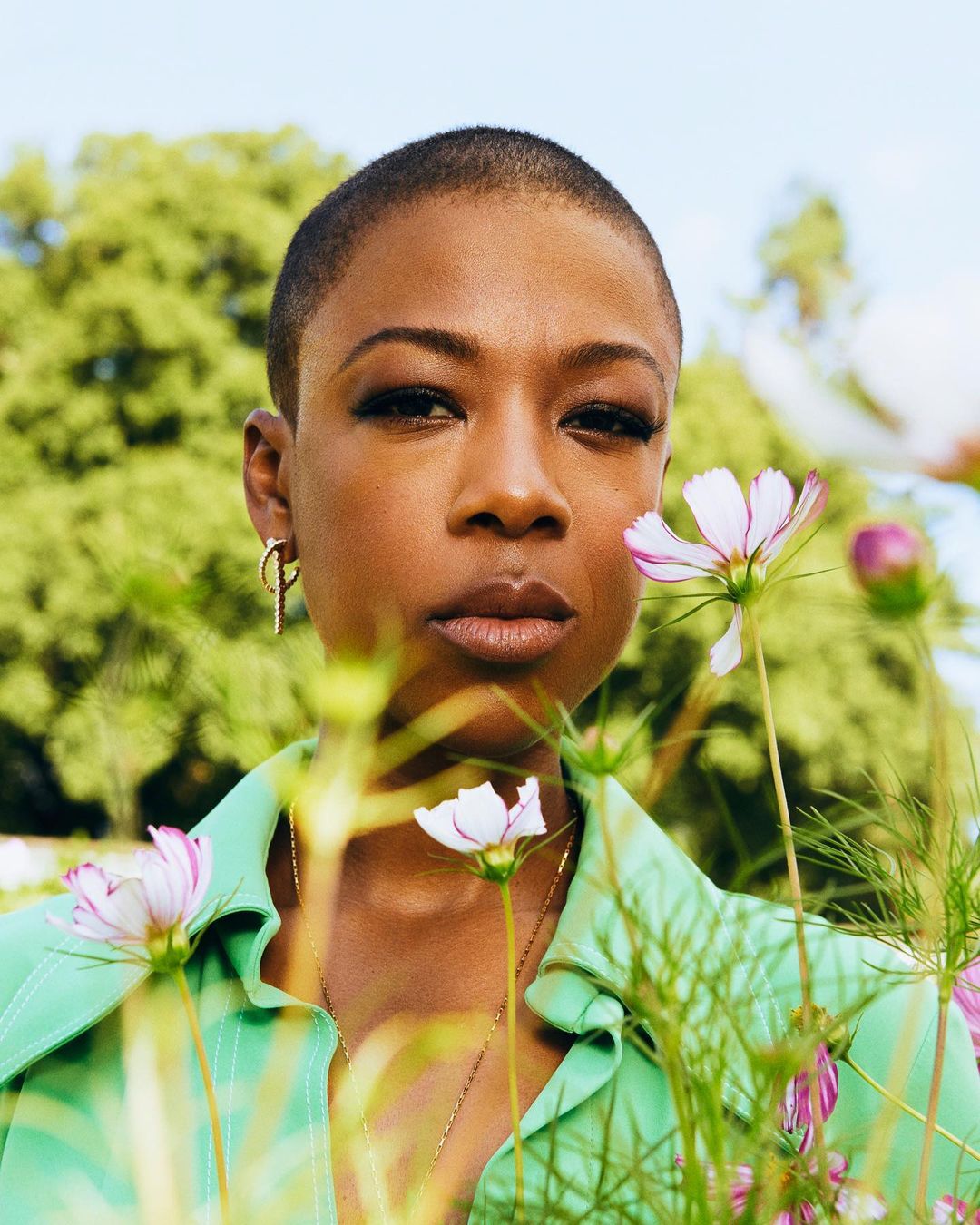 Close-up portrait of an African-American adult woman with short hair and light green shirt standing in a field of pink and white flowers.