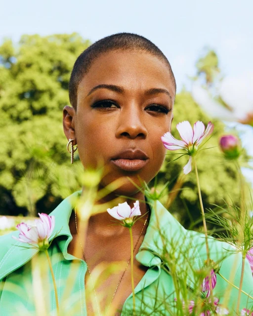 Close-up portrait of an African-American adult woman with short hair and light green shirt standing in a field of pink and white flowers.