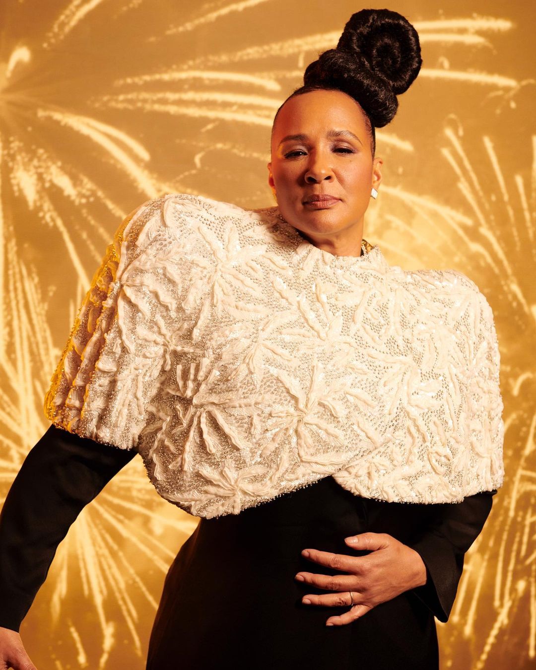 Portrait of an adult woman with an elaborate updo wearing a black dress and textured white shawl, set against a golden firework background.