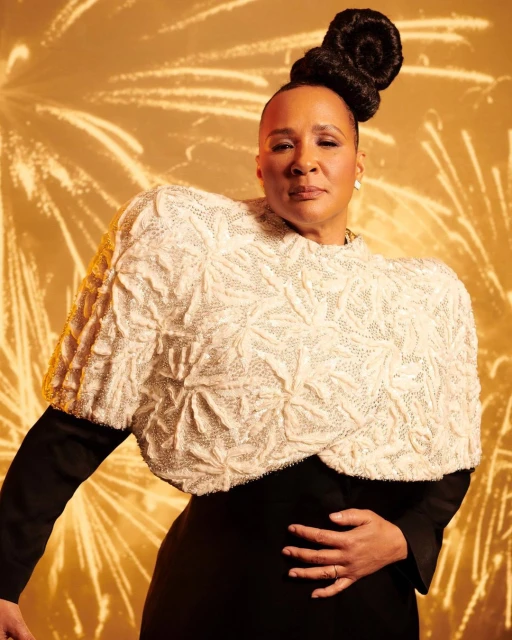 Portrait of an adult woman with an elaborate updo wearing a black dress and textured white shawl, set against a golden firework background.