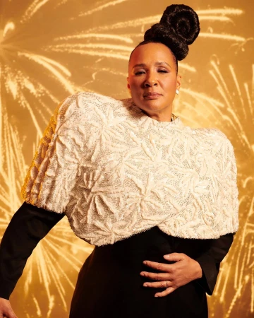 Portrait of an adult woman with an elaborate updo wearing a black dress and textured white shawl, set against a golden firework background.