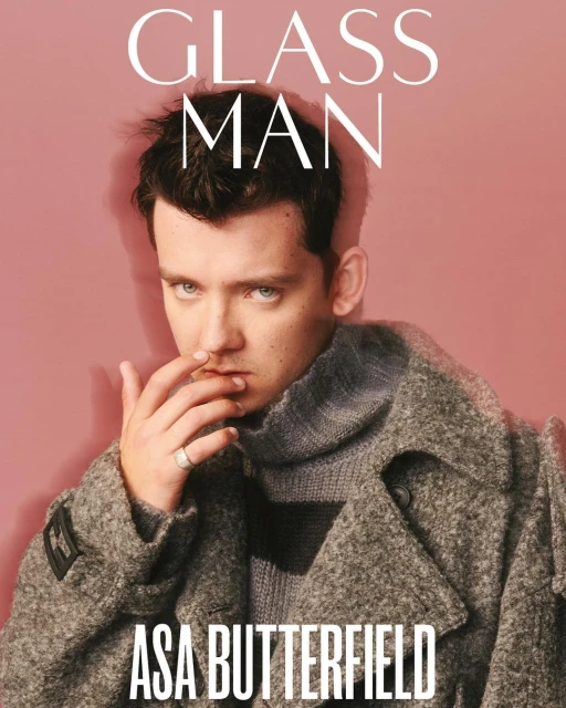 Portrait of Asa Butterfield in a grey coat, with 'Glass Man' magazine text, set against a pale pink background. Fashion and celebrity.