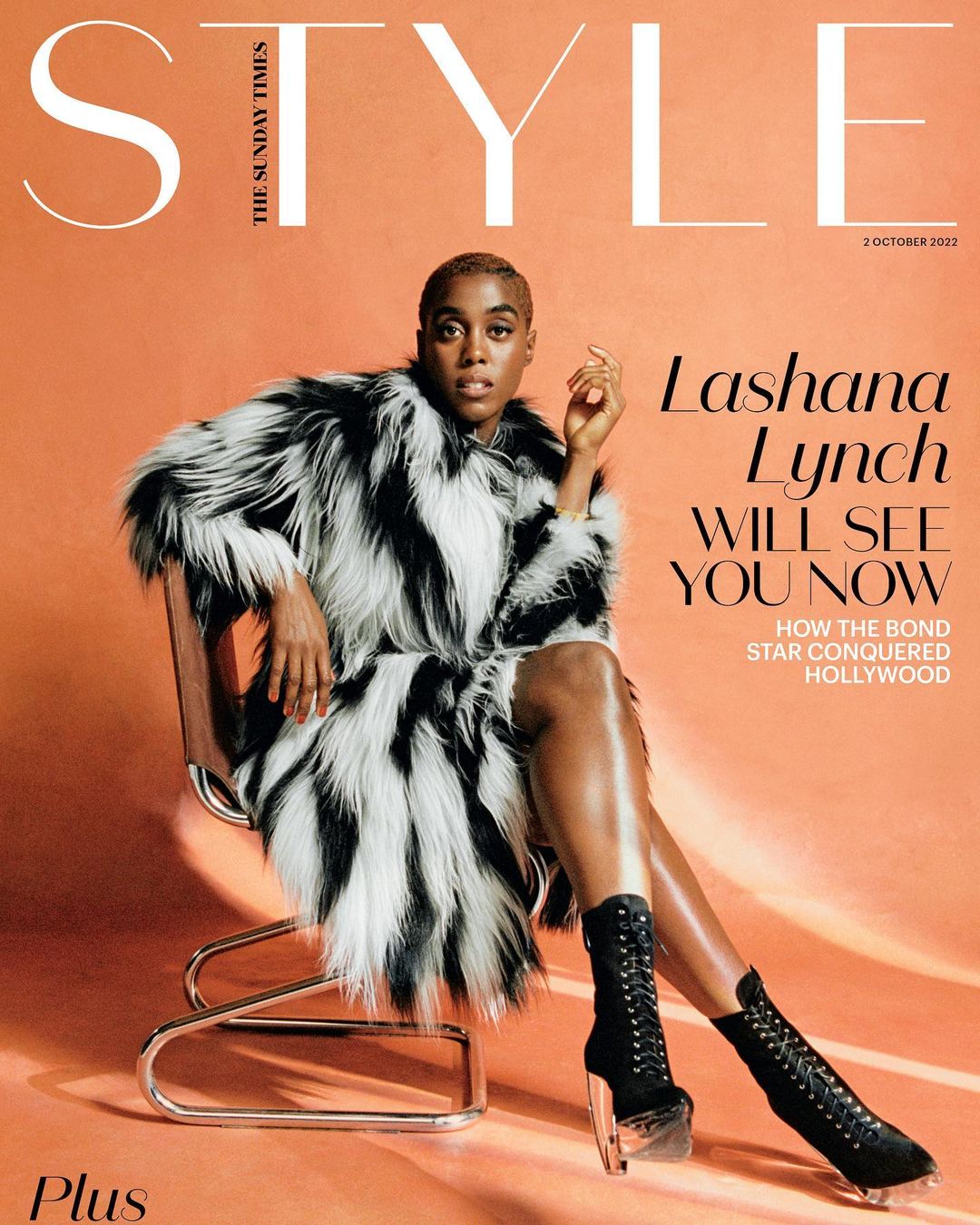 Fashion magazine cover featuring Lashana Lynch in a black and white fur coat and heeled boots, sitting on a chrome chair against a peach backdrop.