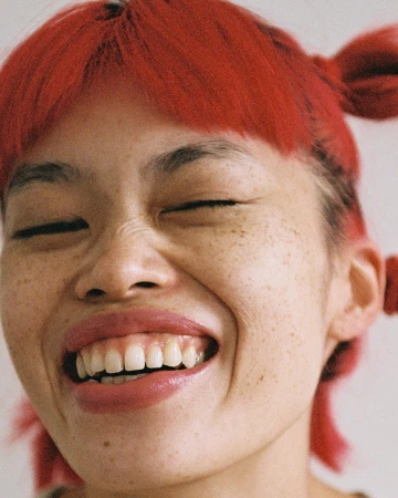Close-up portrait of a laughing young woman with bright red hair and heavy freckles captured by Rosaline Shahnavaz