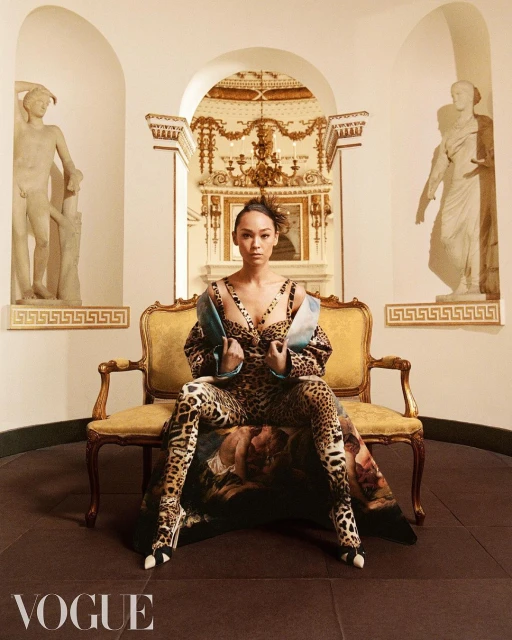 Woman in leopard print outfit poses on ornate bench in front of statues in a classical interior, captured in a fashion editorial.