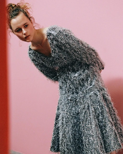 A young woman poses in a sparkly silver dress against a pink backdrop, creating a fashion-forward and visually striking composition.