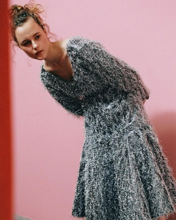 A young woman poses in a sparkly silver dress against a pink backdrop, creating a fashion-forward and visually striking composition.