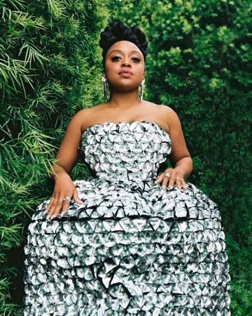 Black woman wearing a strapless metallic silver textured dress standing outdoors against lush green foliage