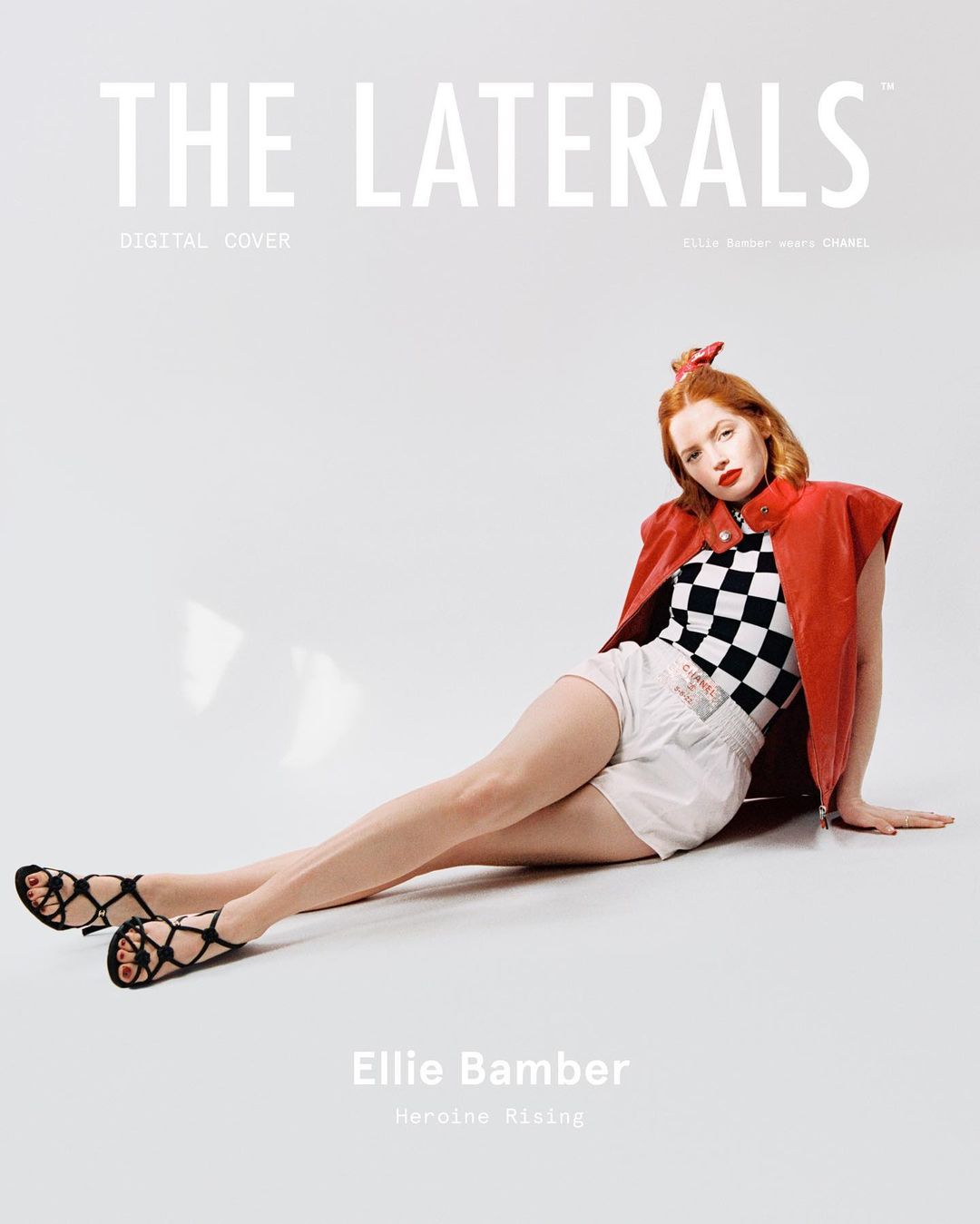 Magazine cover shot of Ellie Bamber wearing a checkerboard top, shorts, and vest, sitting against a white background in a photo studio.