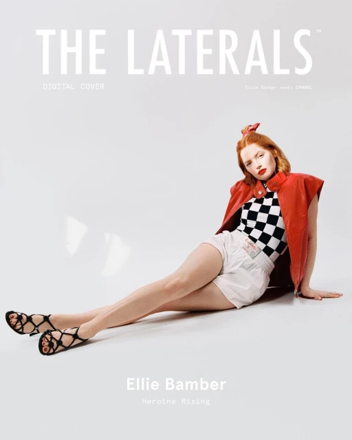 Magazine cover shot of Ellie Bamber wearing a checkerboard top, shorts, and vest, sitting against a white background in a photo studio.