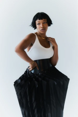 Portrait of a Black woman in a white tank top and wide black skirt photographed by Rosaline Shahnavaz against a white background.