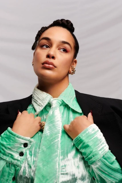 Close-up portrait of an adult woman with an updo, wearing a mint-green velvet shirt with a tie, and a black blazer in a studio.