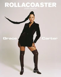 Portrait of singer Grace Carter wearing a black blazer dress and tall brown boots against a grey studio backdrop by Rosaline Shahnavaz.