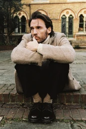 Man crouching on brick steps wearing a tweed blazer, turtleneck, and dark trousers photographed by Rosaline Shahnavaz