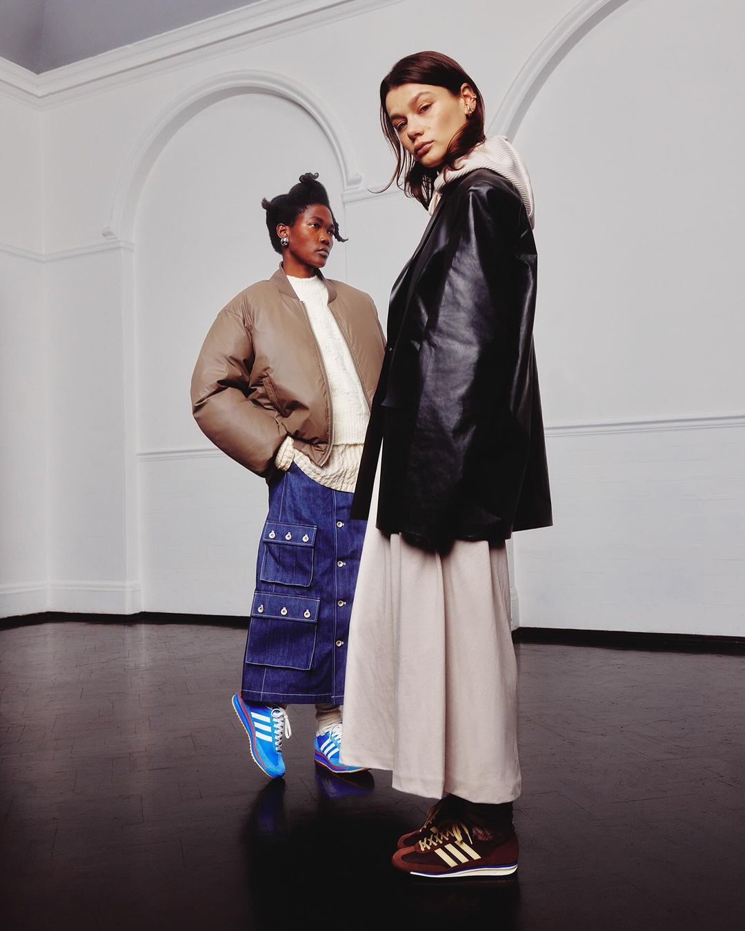 Two women in a photo studio wearing streetwear fashion, one in a jacket and skirt, the other in a puffer jacket and cargo skirt.