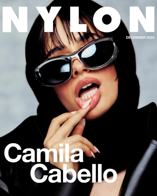 Camila Cabello on Nylon Magazine cover, December 2024 issue, wearing sunglasses and black hooded jacket, with finger touching her lips.