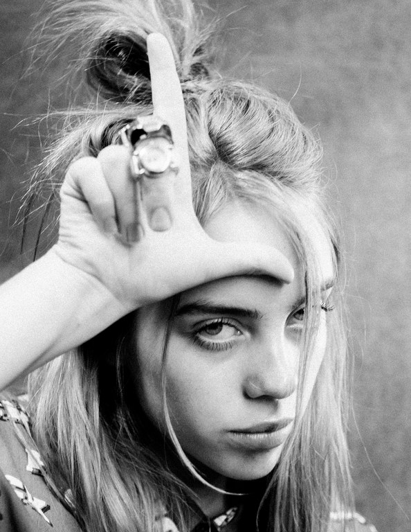 Black and white portrait of a young adult female with blonde hair, wearing a ring and posing with her hand on her forehead.