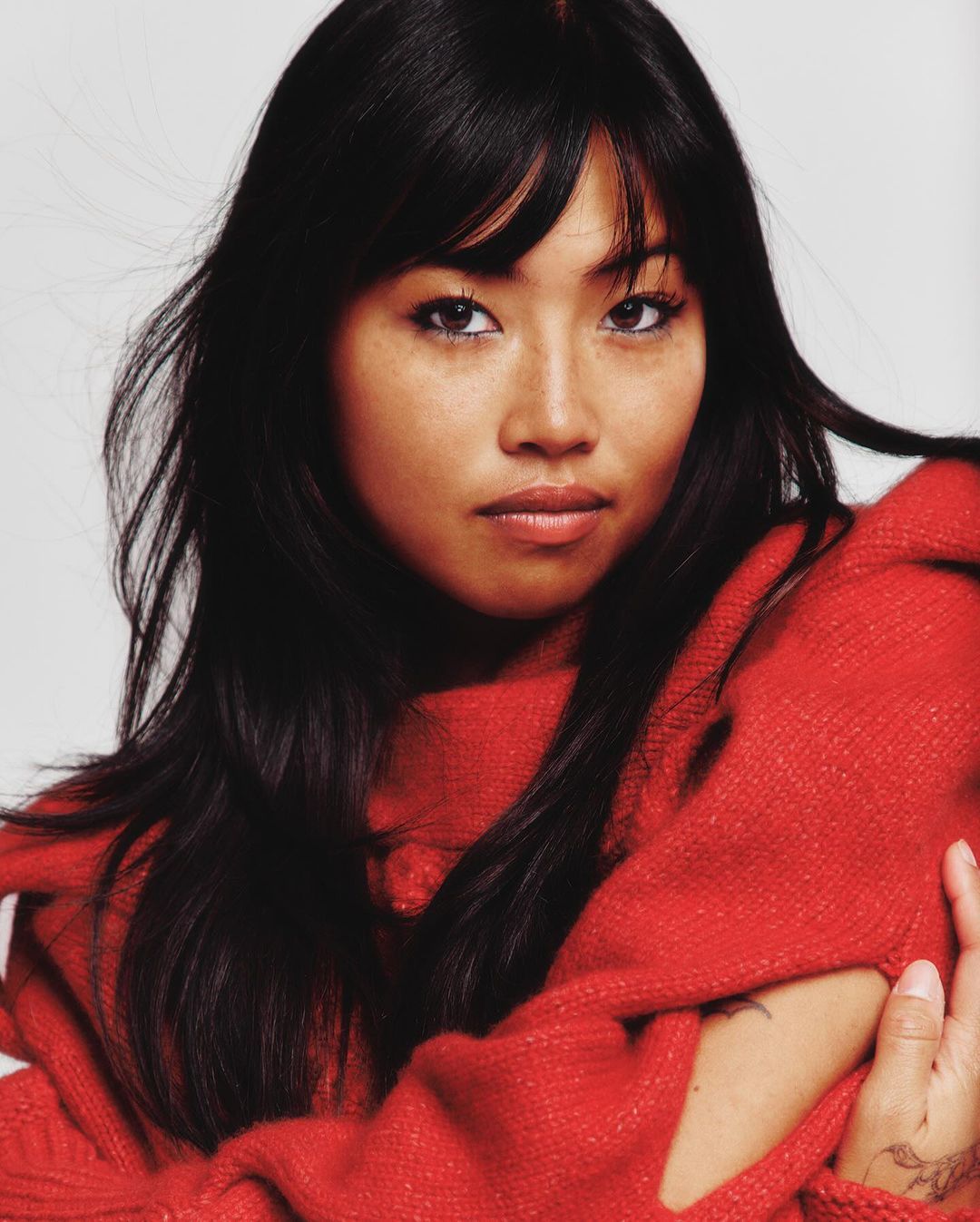 Portrait of a woman with long dark hair wearing a bright red sweater against a neutral background.