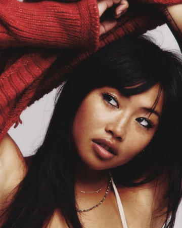 Close-up portrait of a woman with long dark hair lifting arms in a red ribbed sweater by photographer Ryan Saradjola