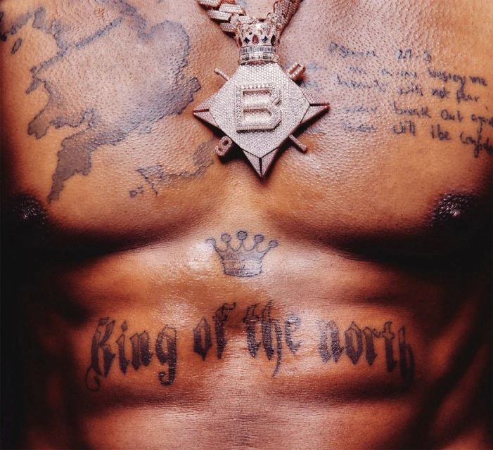 Close-up shot of a dark-skinned man's chest adorned with tattoos and a large diamond pendant, emphasizing texture and luxury.