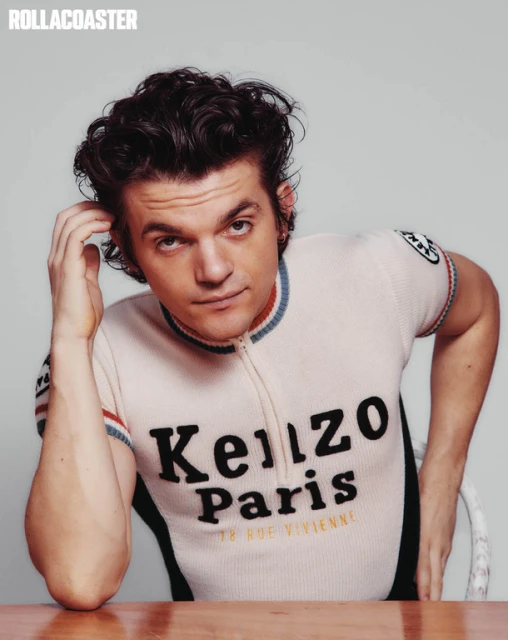 Portrait of an adult male wearing a Kenzo Paris shirt, looking at the camera and touching his hair, inside a photo studio.