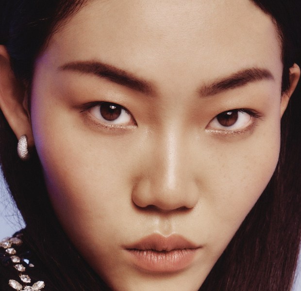 Close-up portrait of a young Asian woman with brown eyes and dark hair, featuring a neutral facial expression, and wearing hoop earrings.
