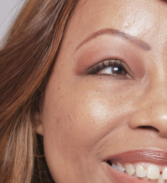 Close-up portrait of a woman's face highlighting her eye makeup, freckles, and smiling expression