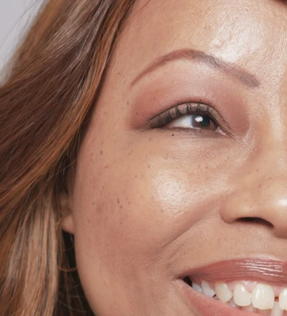 Close-up portrait of a woman's face highlighting her eye makeup, freckles, and smiling expression
