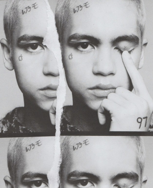Monochromatic portrait of a young adult with face tattoos split by a torn paper effect, showcasing a pensive and raw aesthetic.
