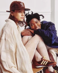 Two women seated together wearing casual apparel, shot by photographer Ryan Saradjola against a neutral interior background.