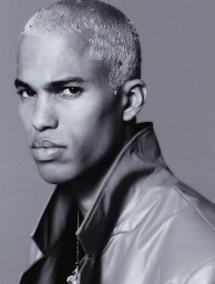 Close-up portrait of a man with short bleached hair adorned with small crystals, wearing a high-collared jacket.