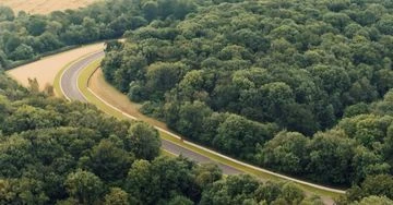 Aerial view of a curved asphalt road winding through dense green forest and trees, emphasizing nature and transportation.