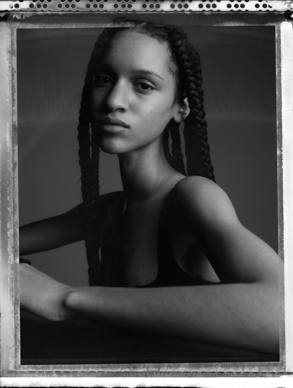 Monochrome portrait of a young woman with braided hair, posing indoors with a serene expression, emphasizing texture and natural beauty.