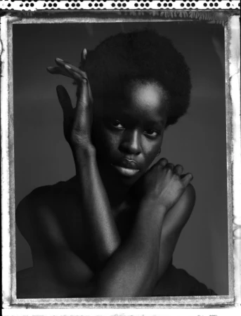 Black and white portrait of a woman with short dark hair, posing with hands near her face against a dark studio background.