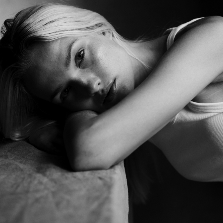 Close-up portrait of a blonde woman resting her head on her arms in monochrome