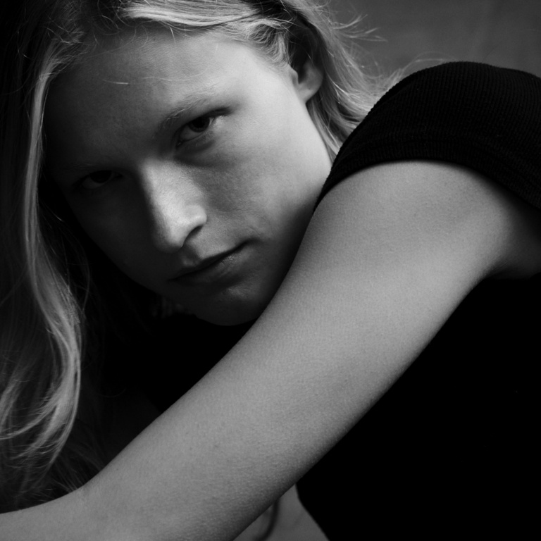 Close-up monochrome portrait of a blonde woman looking directly at the camera with a serious expression, photographed by Victor Demarchelier.