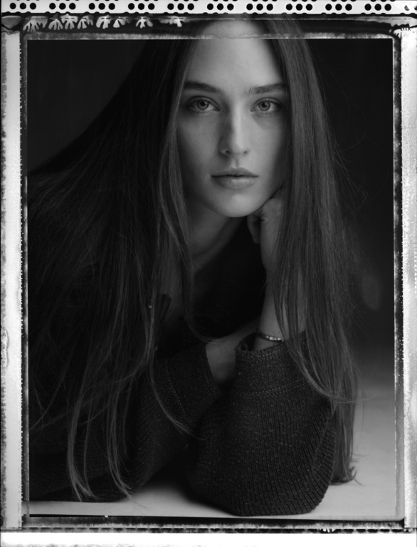 Black and white portrait of a young woman with long hair resting her face on her hand. She is wearing a dark top.