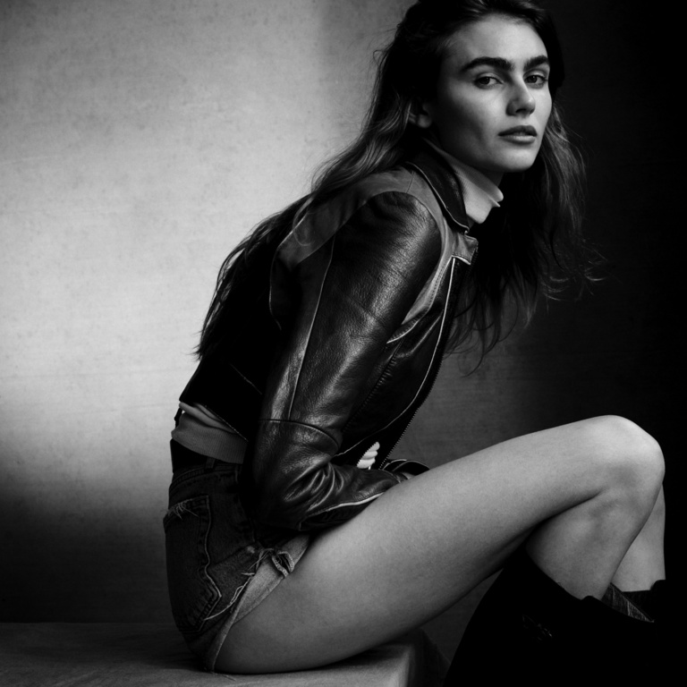 Model in leather jacket seated against a textured background photographed by Victor Demarchelier