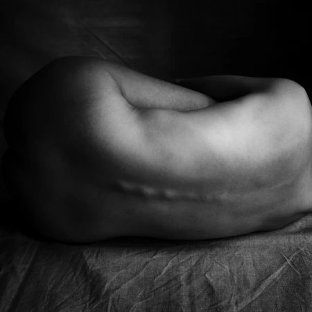 Monochrome shot of a reclining adult human torso, emphasizing skin texture and subtle shadows, captured in a dimly lit setting.