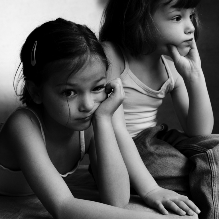 Two young girls resting their chins on their hands in a black and white portrait by Victor Demarchelier.