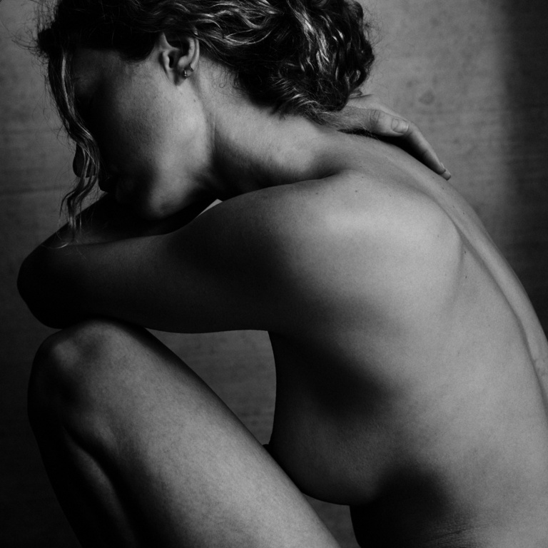 Monochrome portrait of a woman kneeling with her head resting on her arms against a textured concrete background