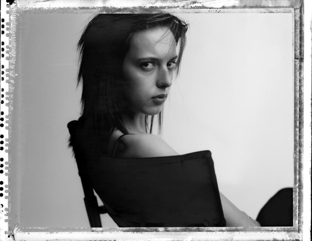 Monochrome portrait of a woman looking back over her shoulder while seated in a chair against a plain light background
