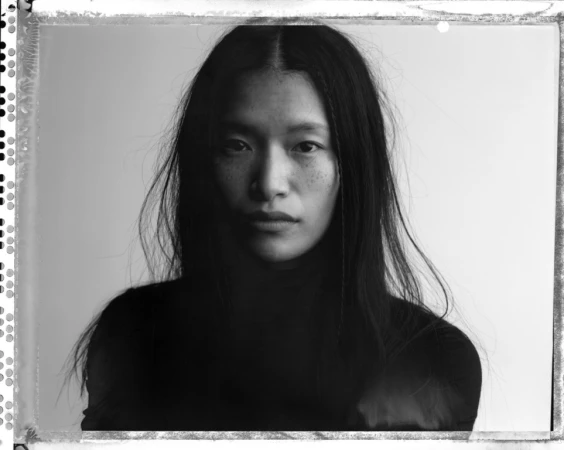 Monochrome portrait of an Asian woman with long dark hair against a plain white background framed by film sprocket holes
