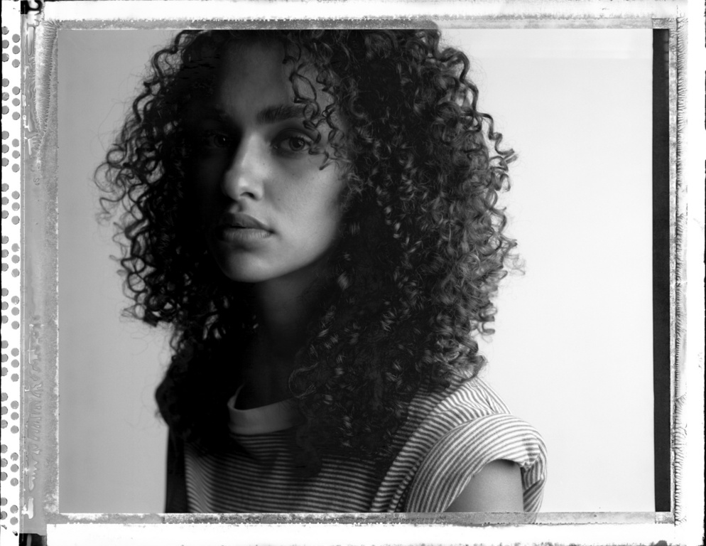 Portrait of a woman with curly hair wearing a striped t shirt against a plain background photographed by Victor Demarchelier