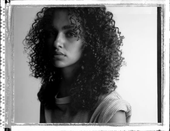 Portrait of a woman with curly hair wearing a striped t shirt against a plain background photographed by Victor Demarchelier